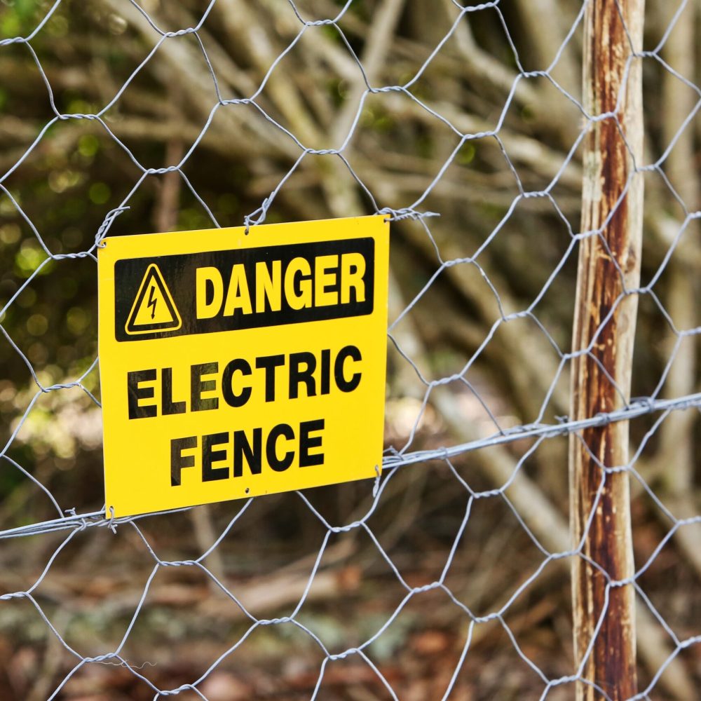 A danger sign hung from the electric fence with the trees in the background