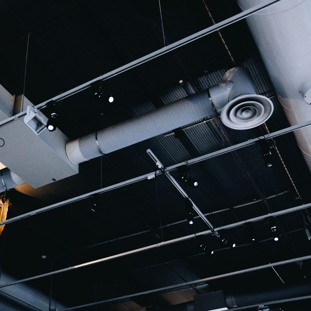 A low angle shot of a metal black ceiling with white ventilation pipes